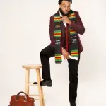 Herzing graduate posing with one foot on a stool in his cap and sash.